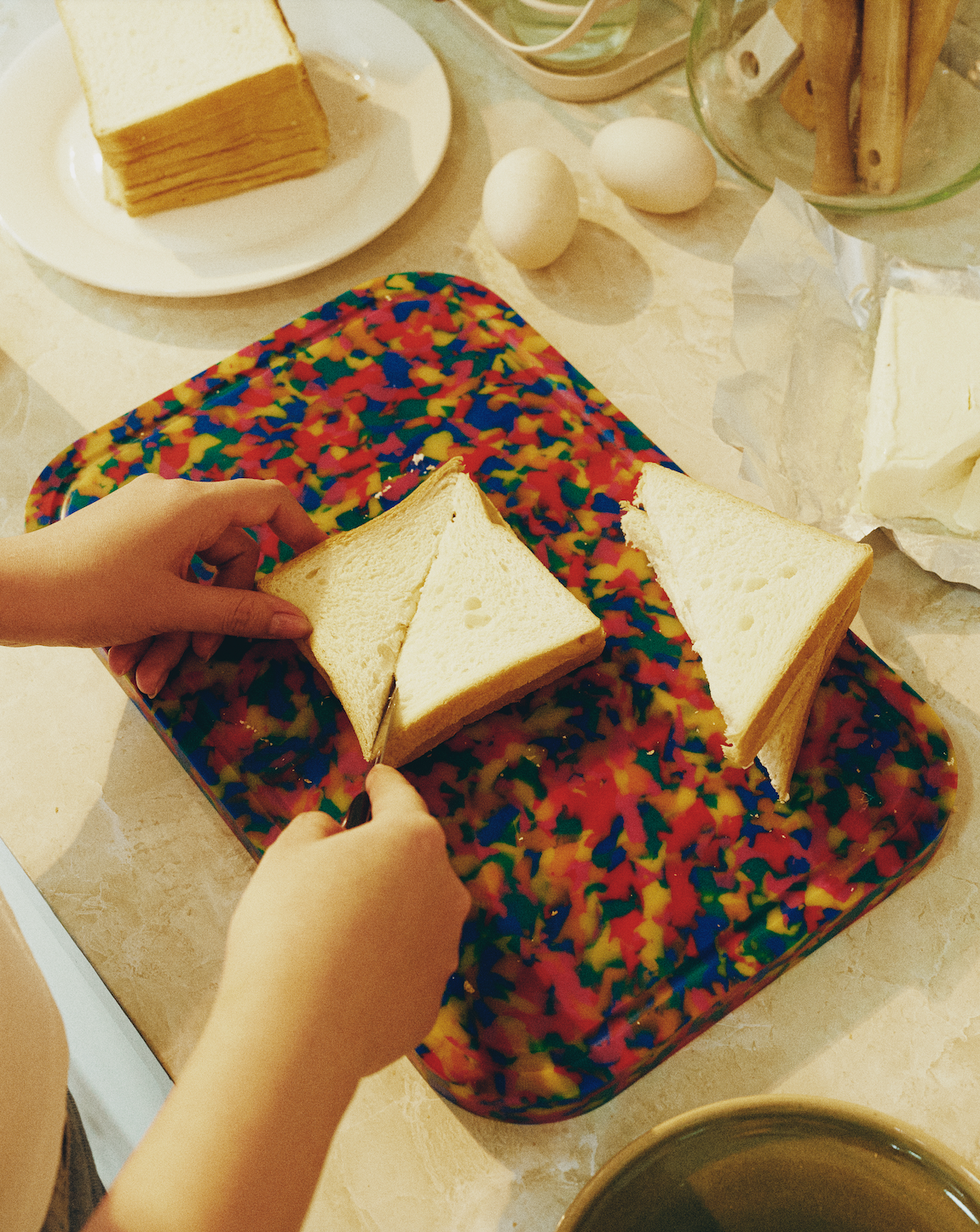 Hands slicing bread on the Carnival cutting board with multicolour confetti design