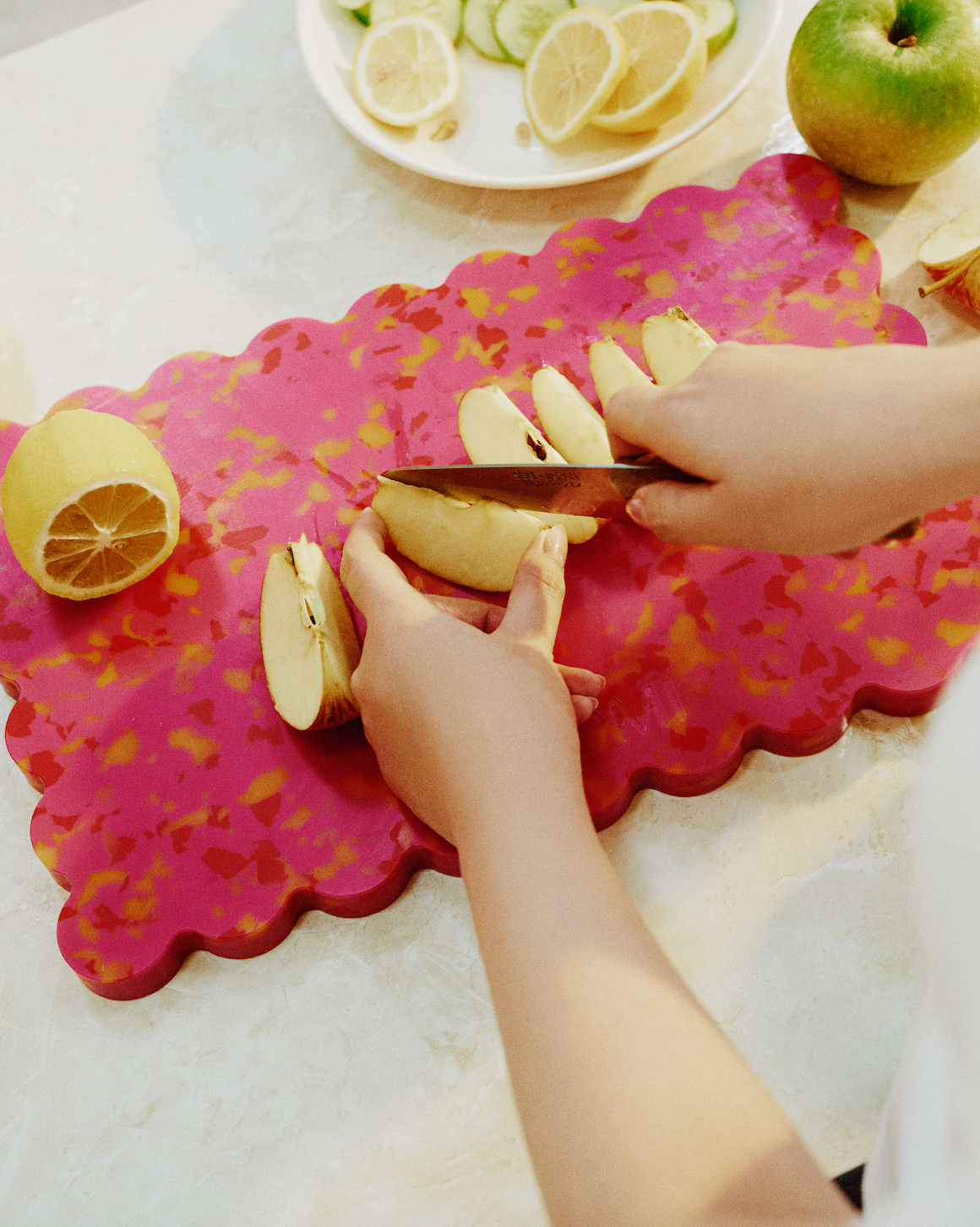 Cherry scalloped cutting board in pink with orange speckles, used for slicing apples