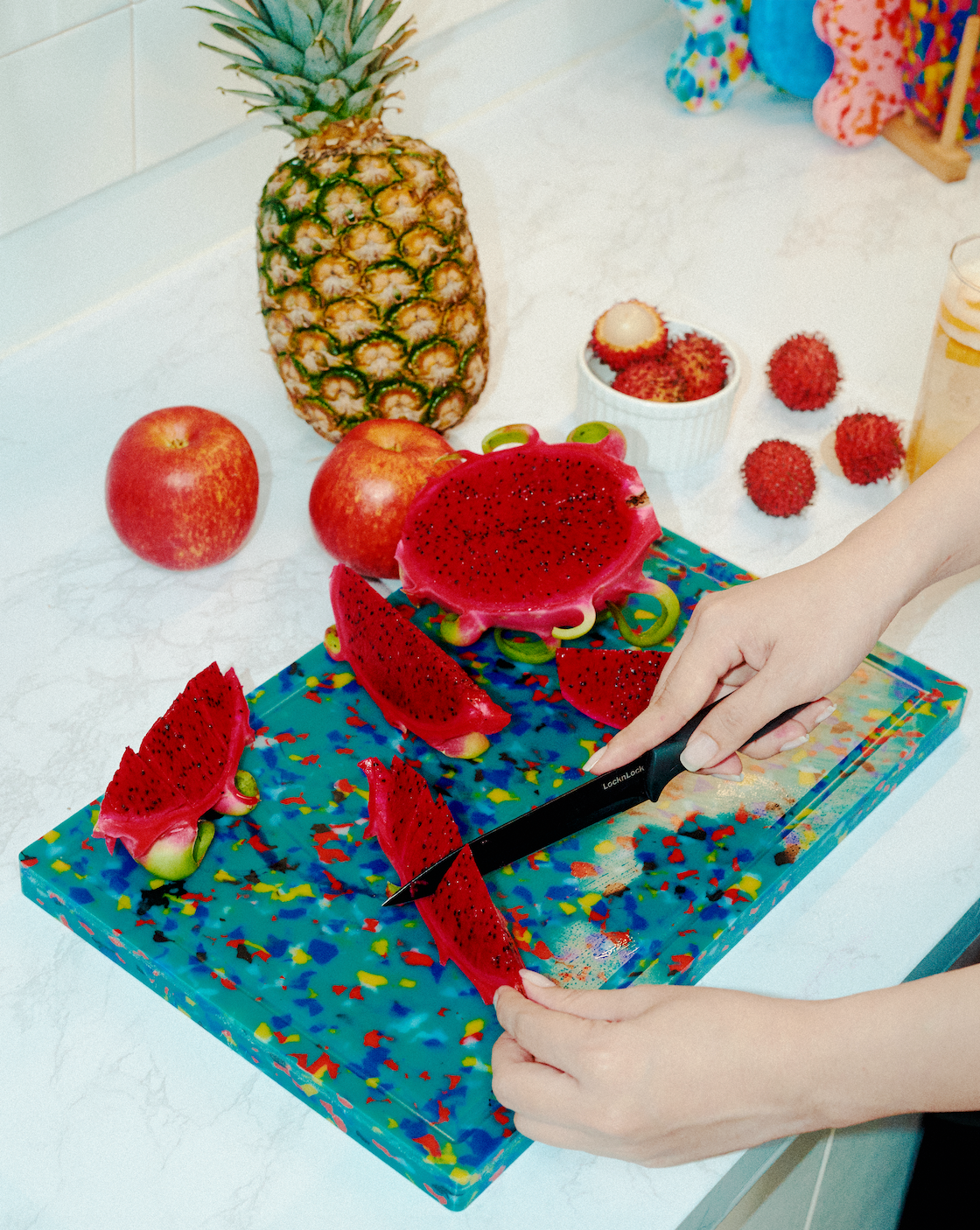 Hands slicing dragon fruit on the Lagoon rectangular cutting board with multicoloured speckles
