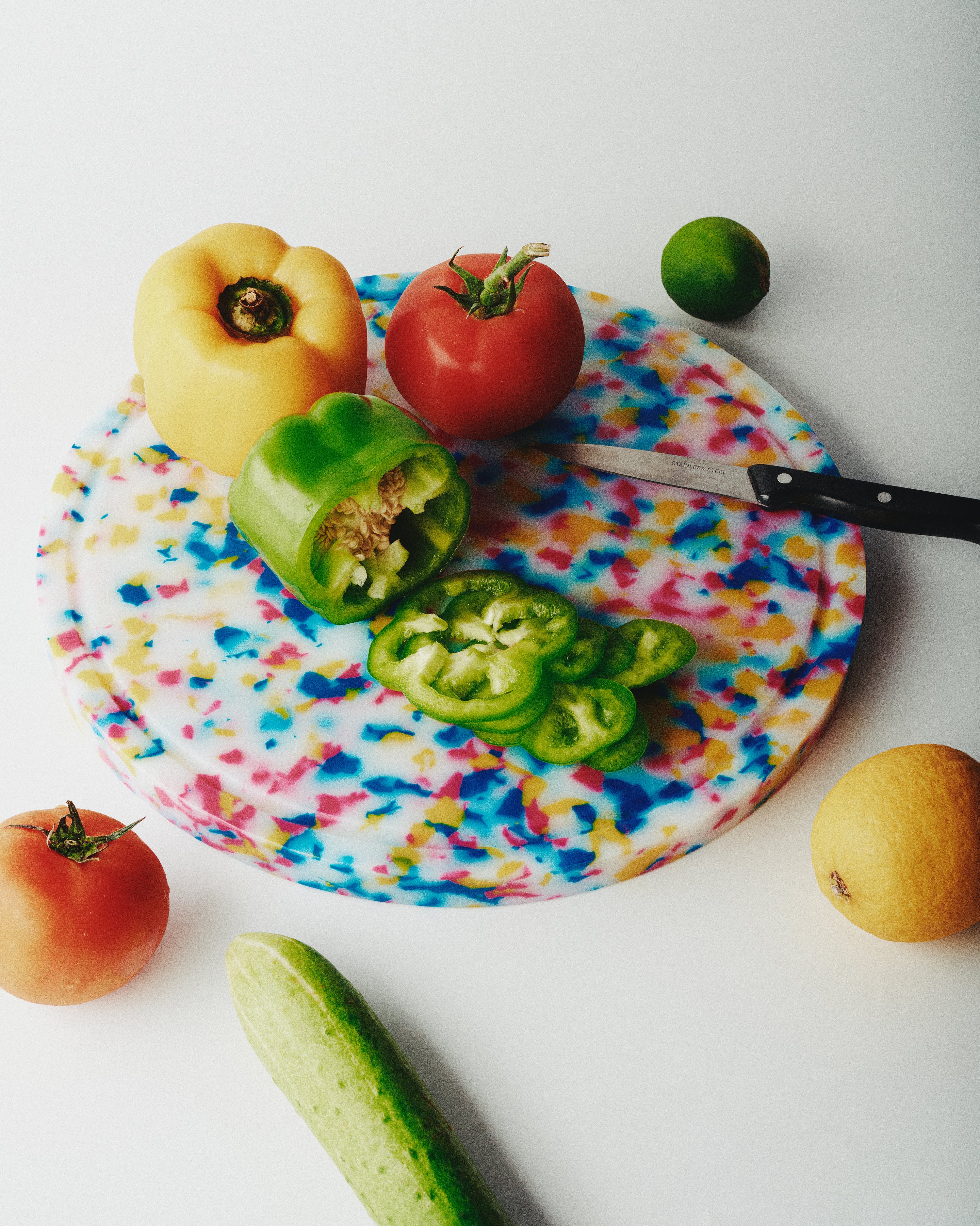 Skye round cutting board with multicoloured speckles, styled with fresh peppers and tomatoes