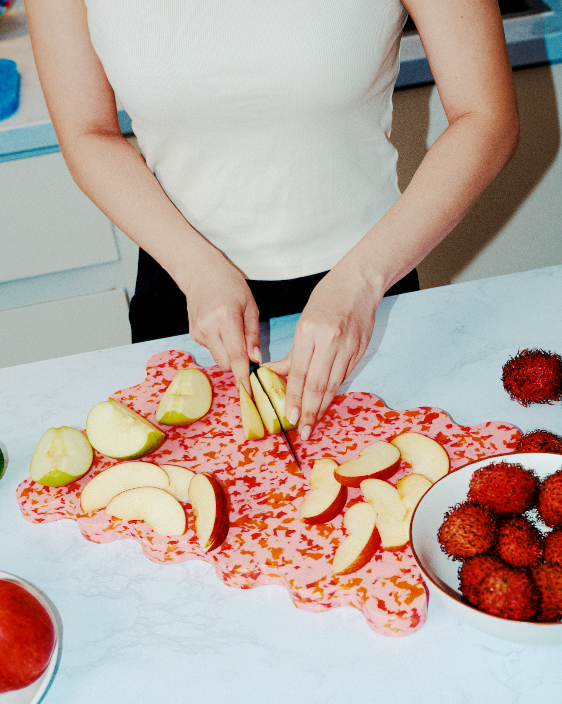 Hands slicing apples on a pink scalloped recycled plastic cutting board with orange and red speckles